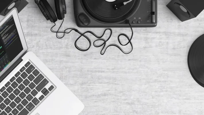 Flat lay van Beginners-DJ-apparatuur: laptop, koptelefoon, draaitafel en speakers op een bureau