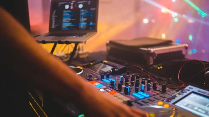 DJ-hand op mixercontroller in levendige club met neonlichten en laptop, promotie voor Virtuele DJ-lessen