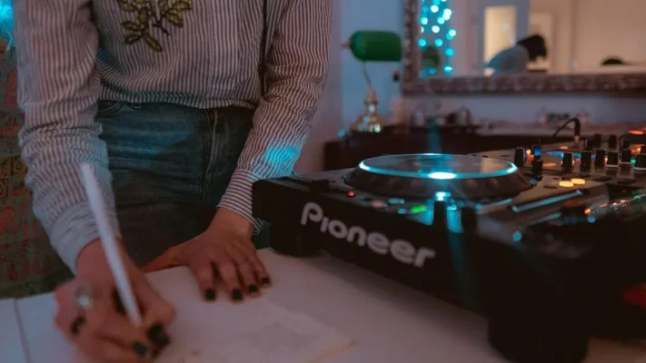 DJ-workshop: DJ met verzorgde nagels maakt aantekeningen naast verlichte audiomixer
