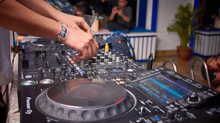 DJ’en op feesten: close-up van DJ-handen op mengpaneel met dansend publiek op de achtergrond