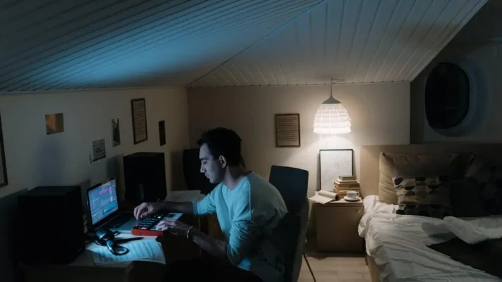 Online DJ-cursus: volwassen man componeert muziek in een gezellige thuisstudio met laptop en synthesizer